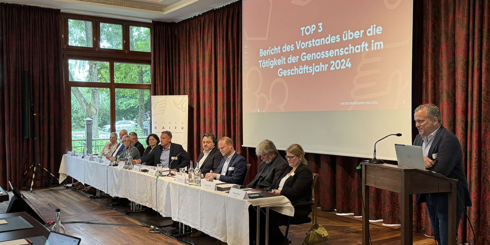 Dennis Voss, Vorstand der KAIFU, steht am Rednerpult und stellt den kaufmännischen Bericht  des Vorstands vor