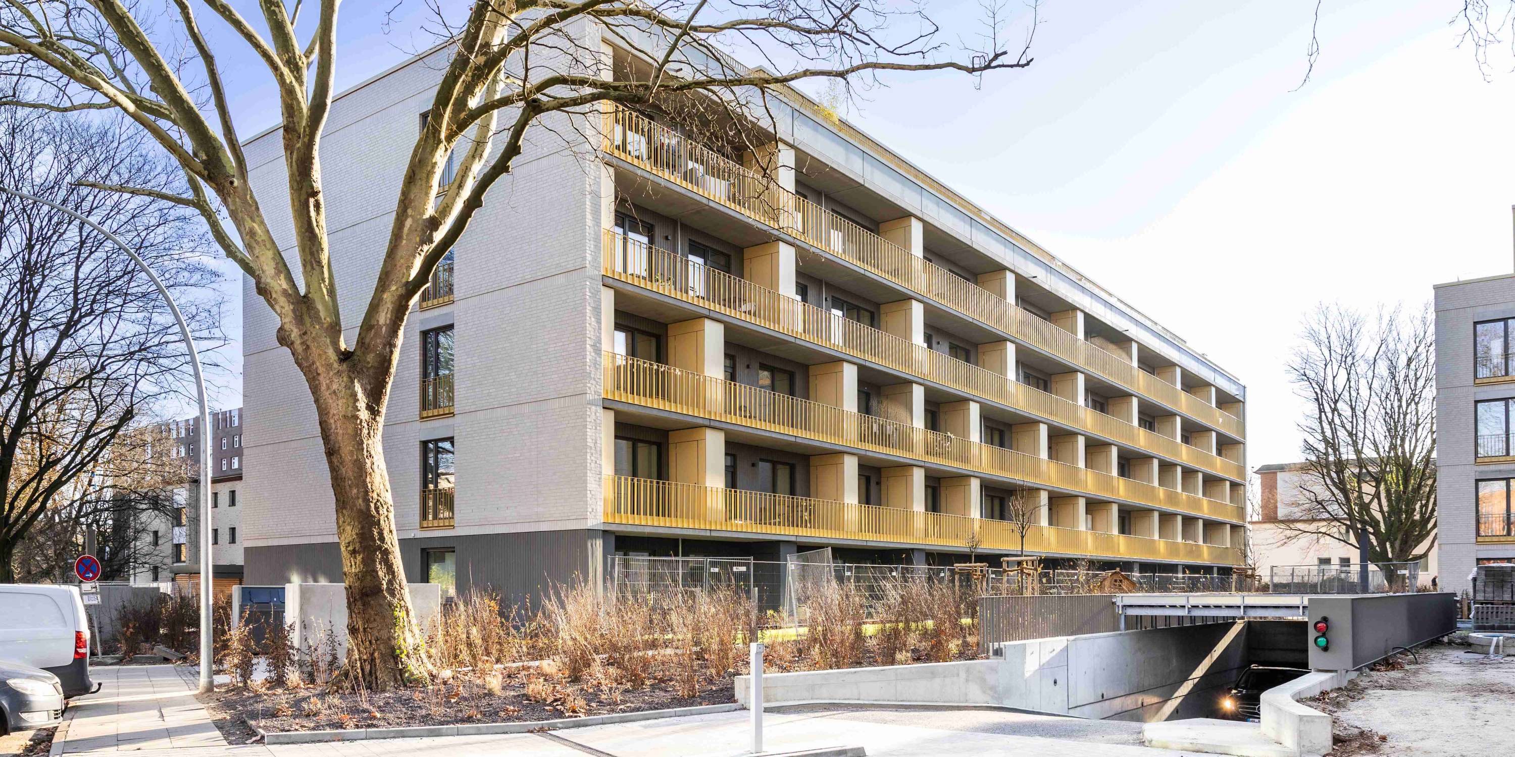Frontalansicht eines modernen, zweistöckigen Mehrfamilienhauses mit weißer Putzfassade und anthrazitfarbenen Fensterrahmen unter blauem Himmel.