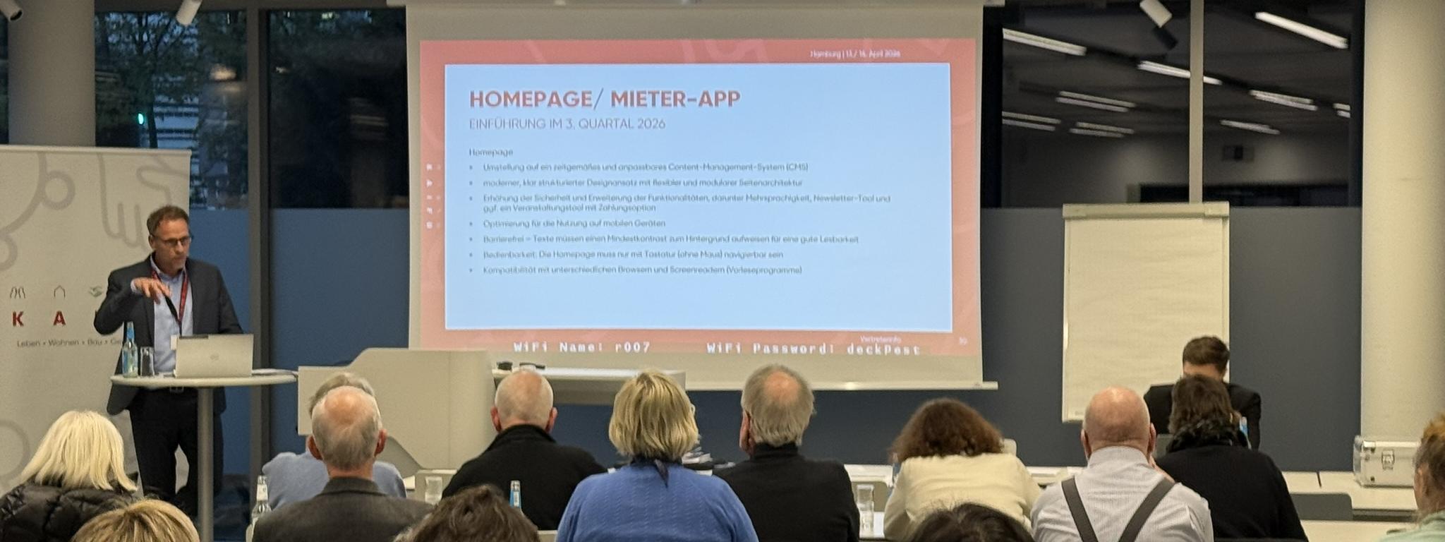 Man sieht Stefan henze, der einen Vortrag vor den Vertretern der KAIFU hält, die im Plenum sitzen